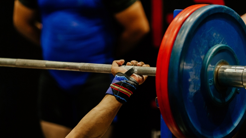 A powerlifter grips a loaded barbell with chalked hands and wrist wraps before a bench press attempt