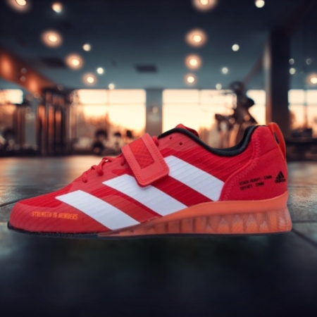 Red Adidas Adipower III weightlifting shoe with white stripes, single strap, and raised heel, designed for arch support and flat-footed lifters, shown in a gym setting