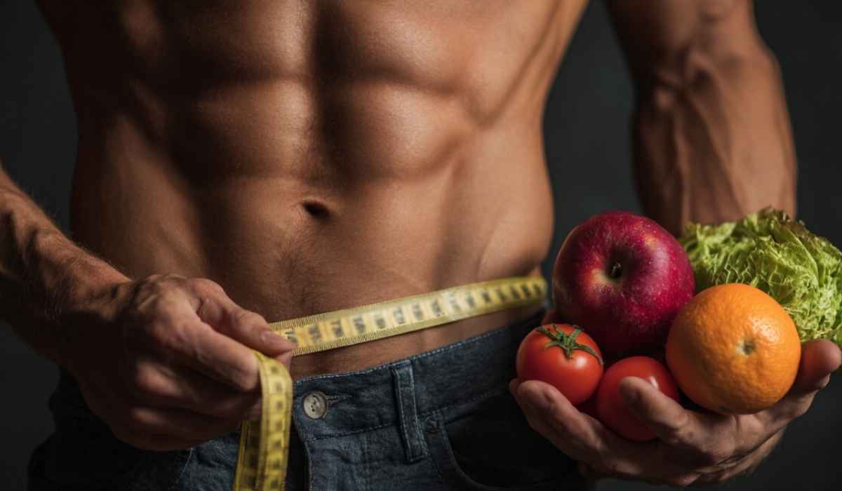 Muscular torso measuring waist while holding fruits and vegetables