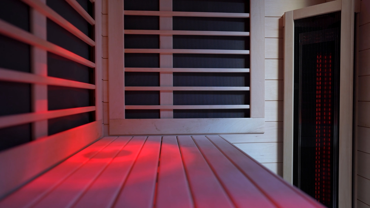 Infrared sauna interior with red light across the wooden bench and heater panels