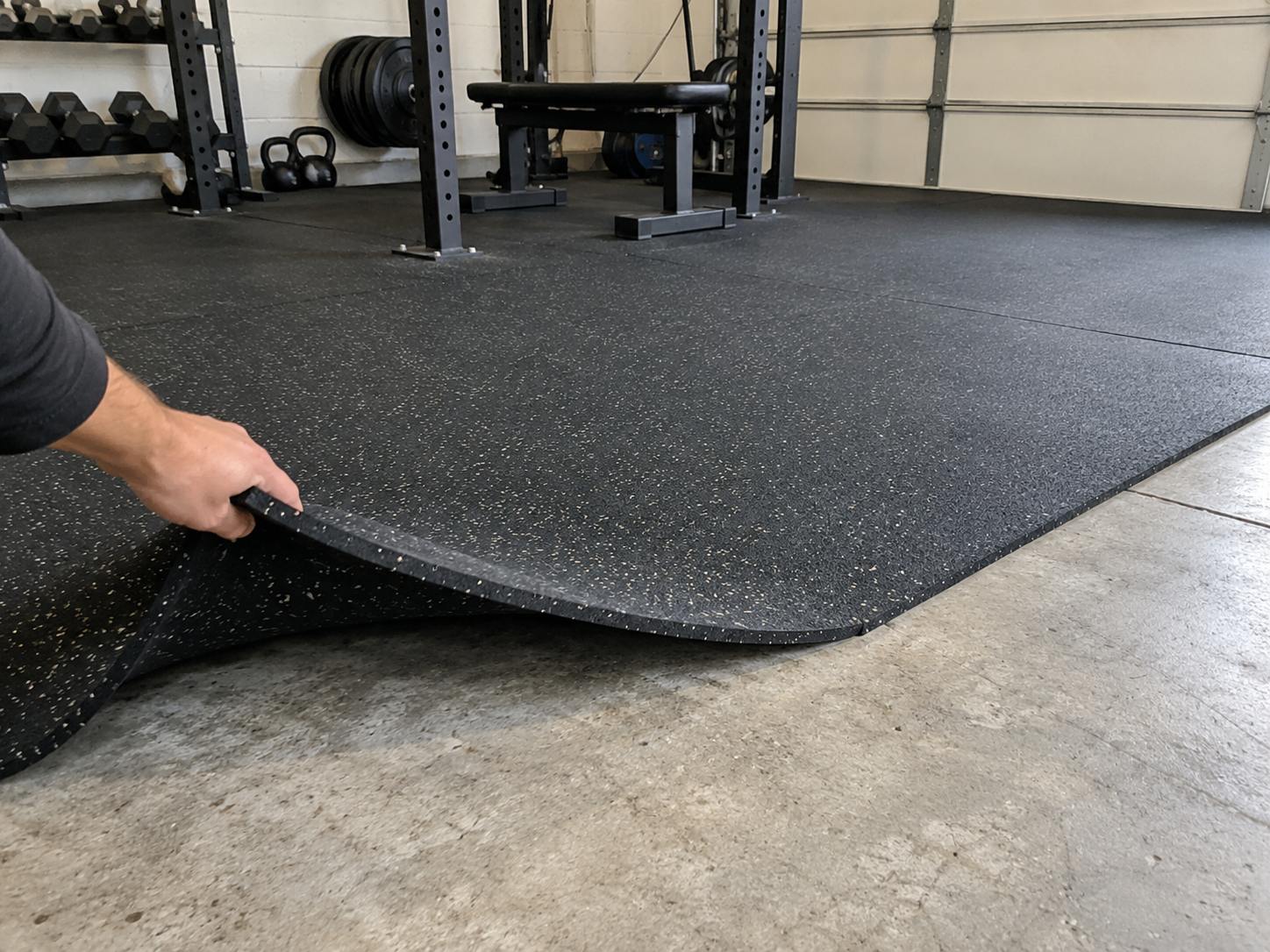 Black rubber gym flooring lifted to reveal the concrete floor underneath.